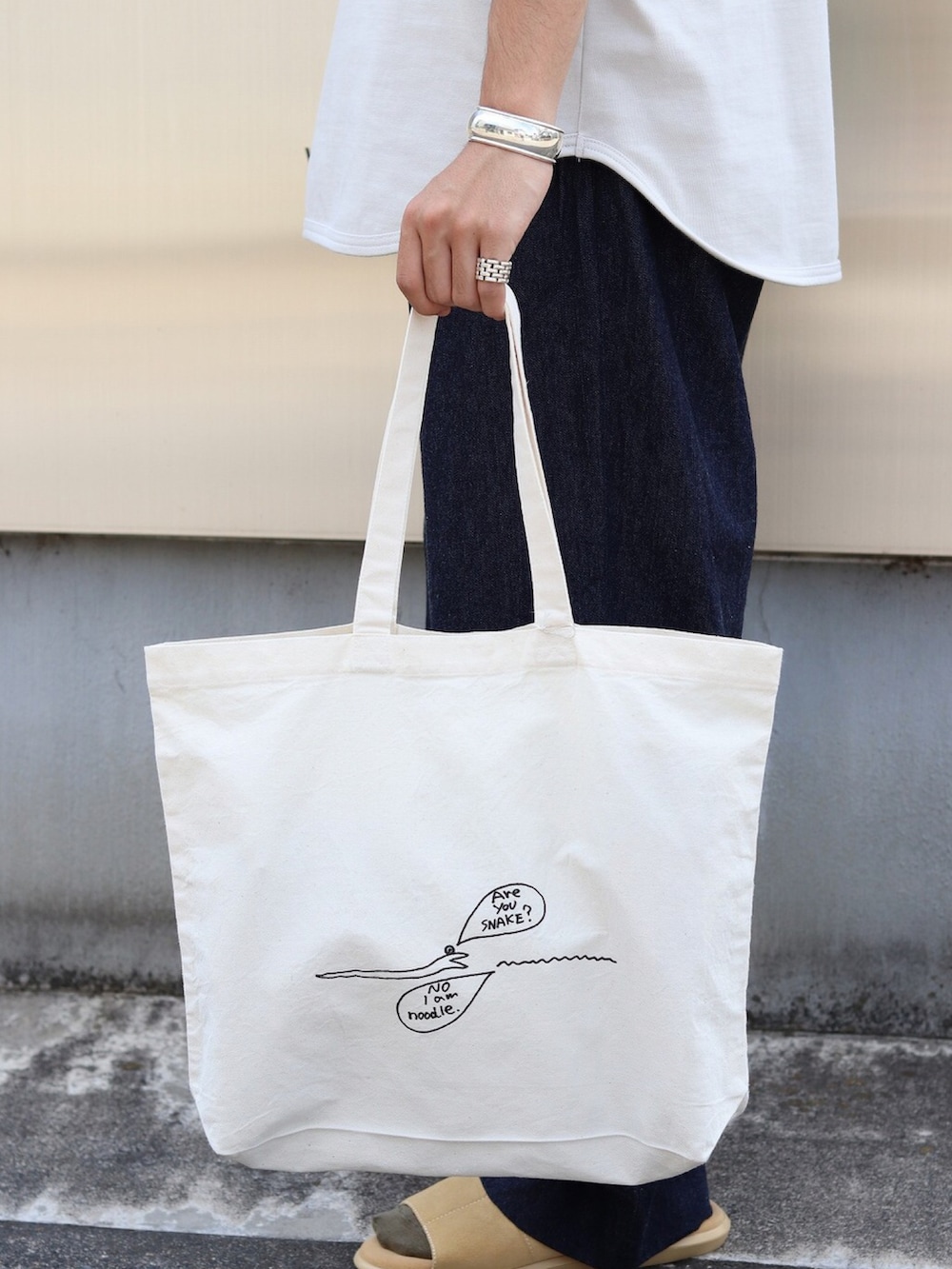 ホワイト系のTシャツ/カットソー、ブラック系のデニムパンツ、ホワイト系のトートバッグを着用したメンズの夏コーディネートの4枚目の写真