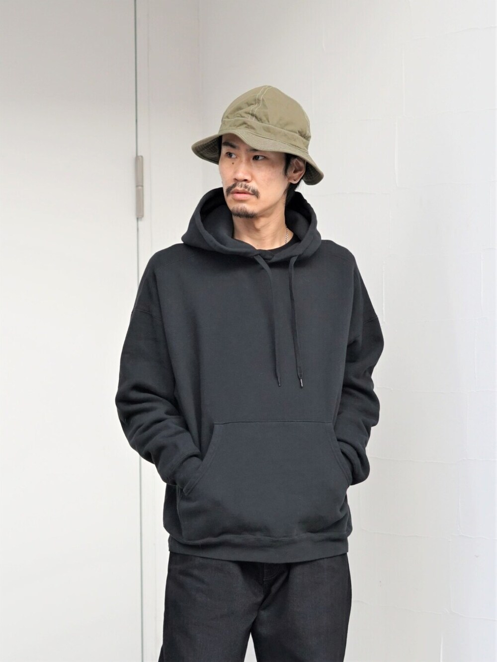 グリーン系のジャケット/アウター、ブラック系のパーカー、ブラック系のデニムパンツを着用したメンズの冬コーディネートの2枚目の写真