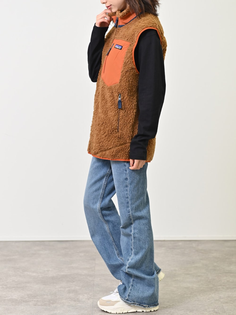 ブラウン系のダウンベスト、ブルー系のデニムパンツ、ホワイト系のスニーカーを着用したレディースの冬コーディネートの2枚目の写真