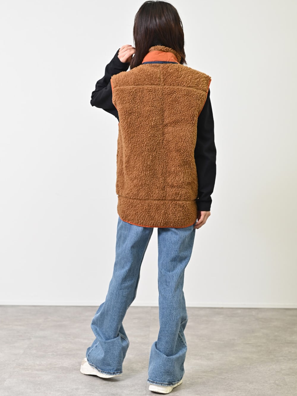 ブラウン系のダウンベスト、ブルー系のデニムパンツ、ホワイト系のスニーカーを着用したレディースの冬コーディネートの3枚目の写真