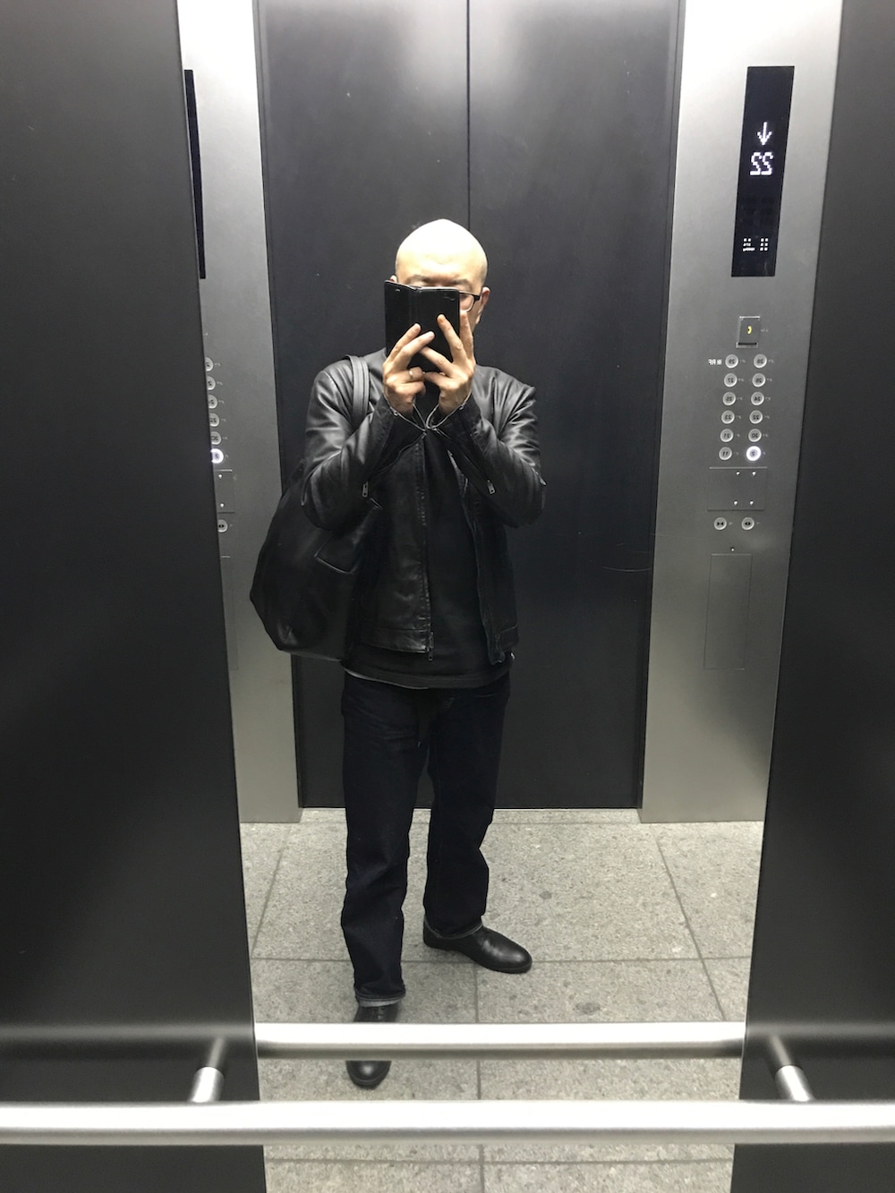 ブラック系のライダースジャケット、ブルー系のデニムパンツ、ブラック系のドレスシューズを着用したメンズの春コーディネートの2枚目の写真