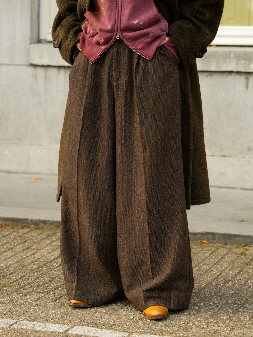 ブラウン系のステンカラーコート、ブラウン系のスラックス、レッド系のパーカーを着用したメンズの秋コーディネートの5枚目の写真