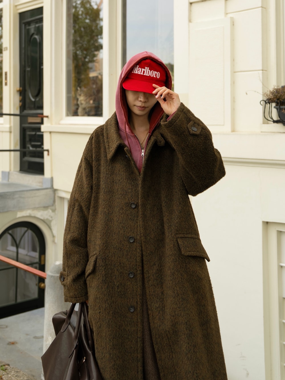 ブラウン系のステンカラーコート、ブラウン系のスラックス、レッド系のパーカーを着用したメンズの秋コーディネートの2枚目の写真