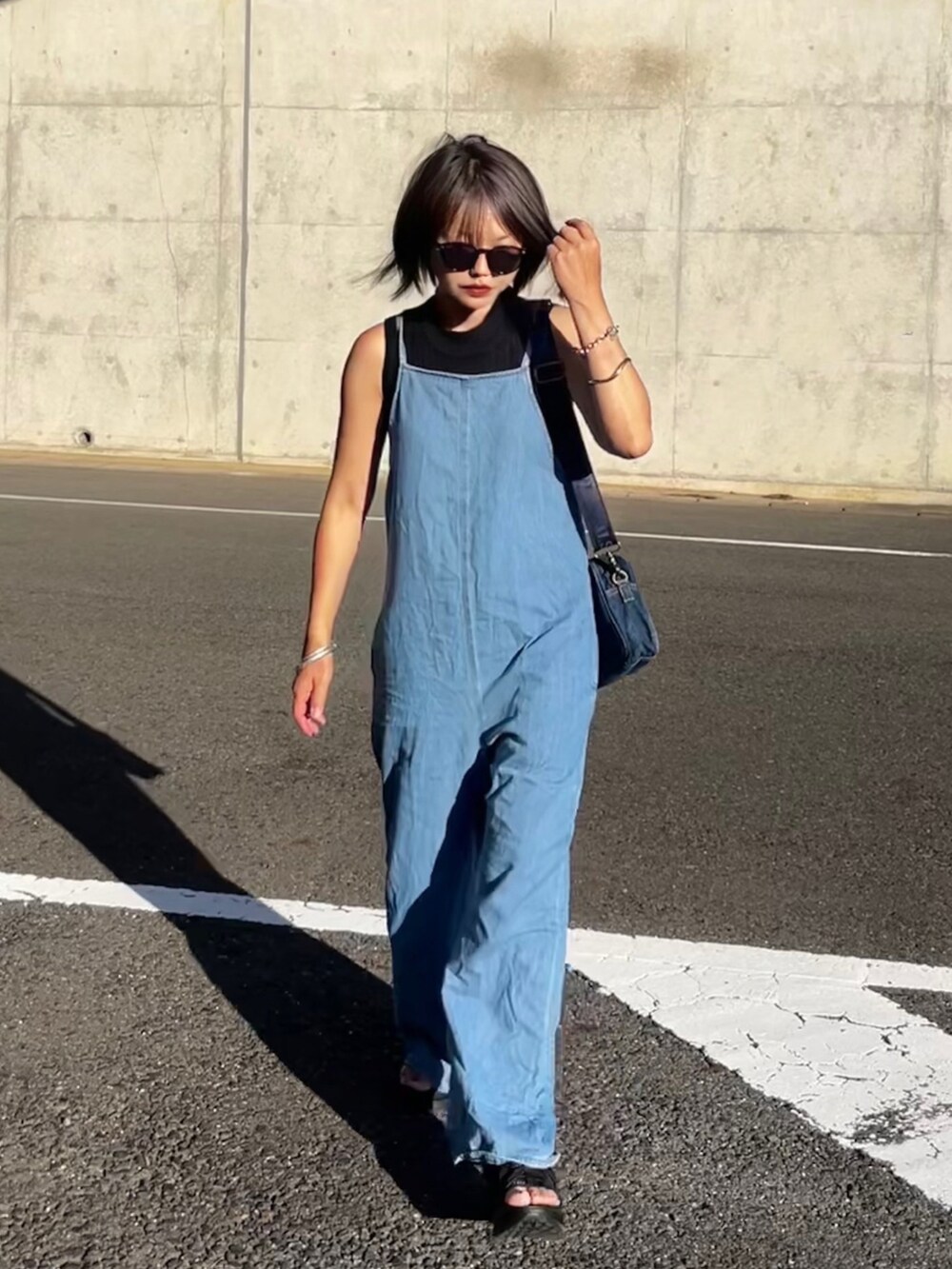ブルー系のサロペット/オーバーオール、ブルー系のショルダーバッグ、ブラック系のサンダルを着用したレディースの夏コーディネートの2枚目の写真