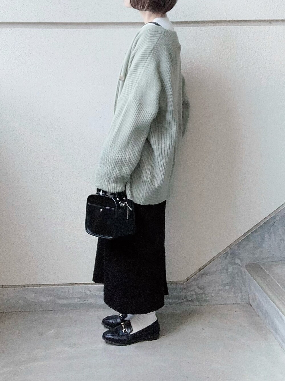 ブラック系のワンピース、グリーン系のカーディガン/ボレロ、ブラック系のトートバッグを着用したレディースの冬コーディネートの2枚目の写真