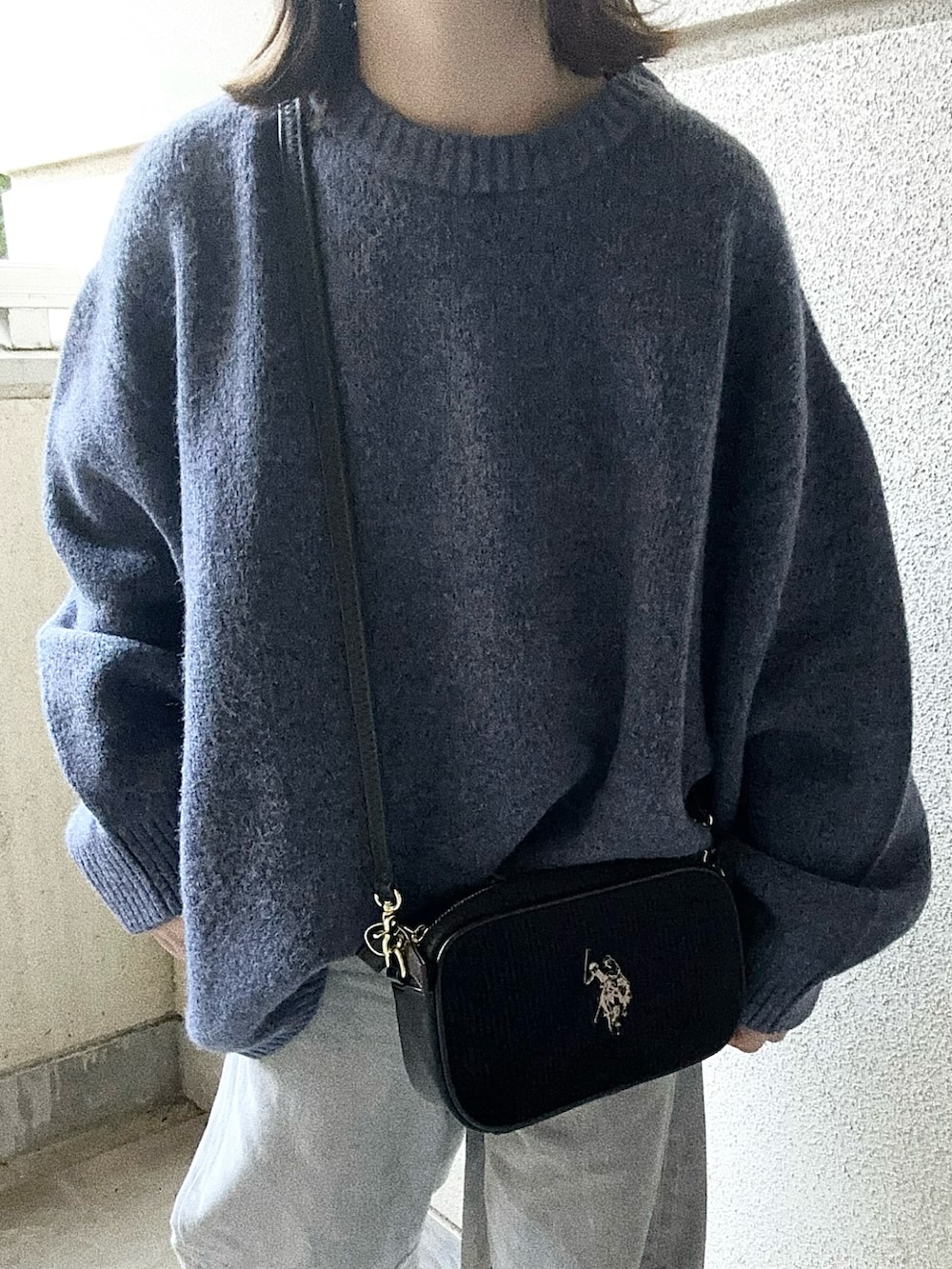 ブラック系のショルダーバッグ、ブルー系のニット/セーター、グレー系のデニムパンツを着用したレディースの秋コーディネートの3枚目の写真