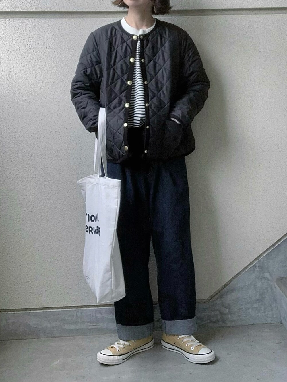 ブラック系のノーカラージャケット、ブルー系のデニムパンツ、ホワイト系のトートバッグを着用したレディースの秋コーディネートの2枚目の写真