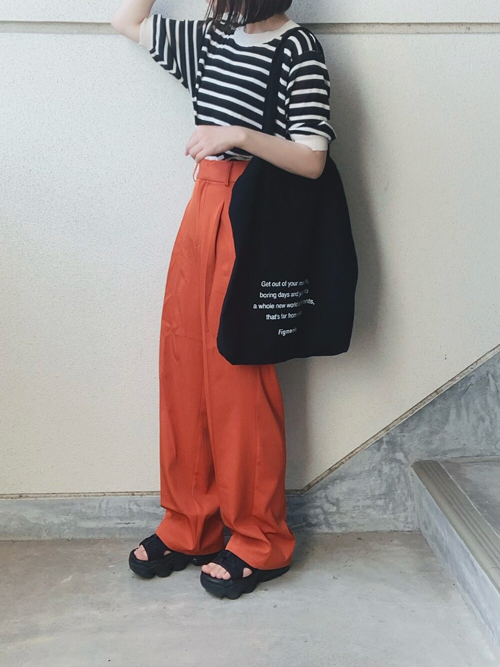 オレンジ系のスラックス、ブラック系のニット/セーター、ブラック系のトートバッグを着用したレディースの夏コーディネートの2枚目の写真