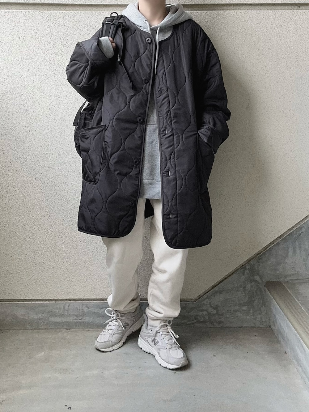 ブラック系のノーカラーコート、グレー系のパーカー、ホワイト系のスウェットパンツを着用したレディースの冬コーディネートの2枚目の写真