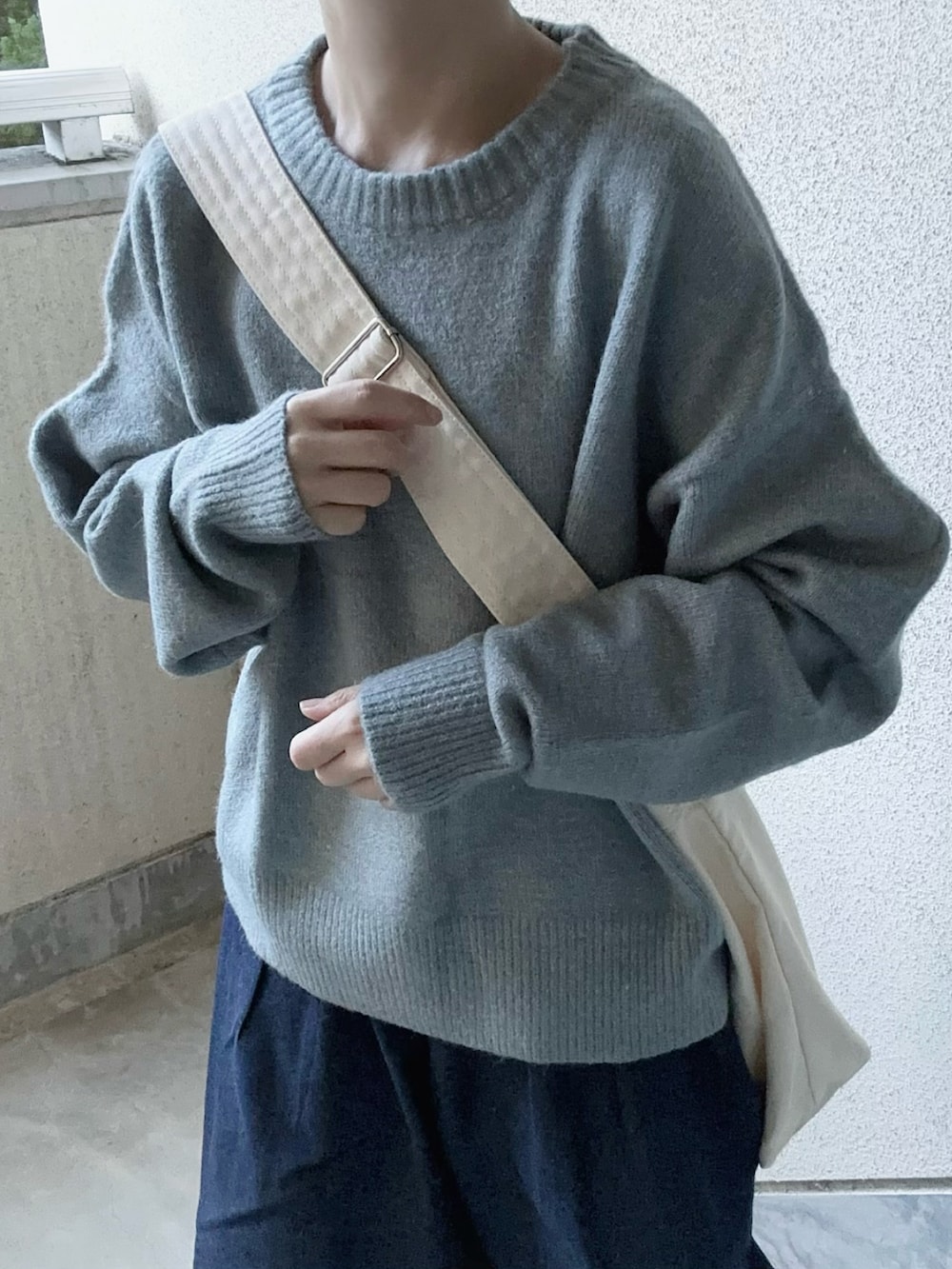 グレー系のニット/セーター、ブルー系のデニムパンツ、ホワイト系のショルダーバッグを着用したレディースの秋コーディネートの3枚目の写真