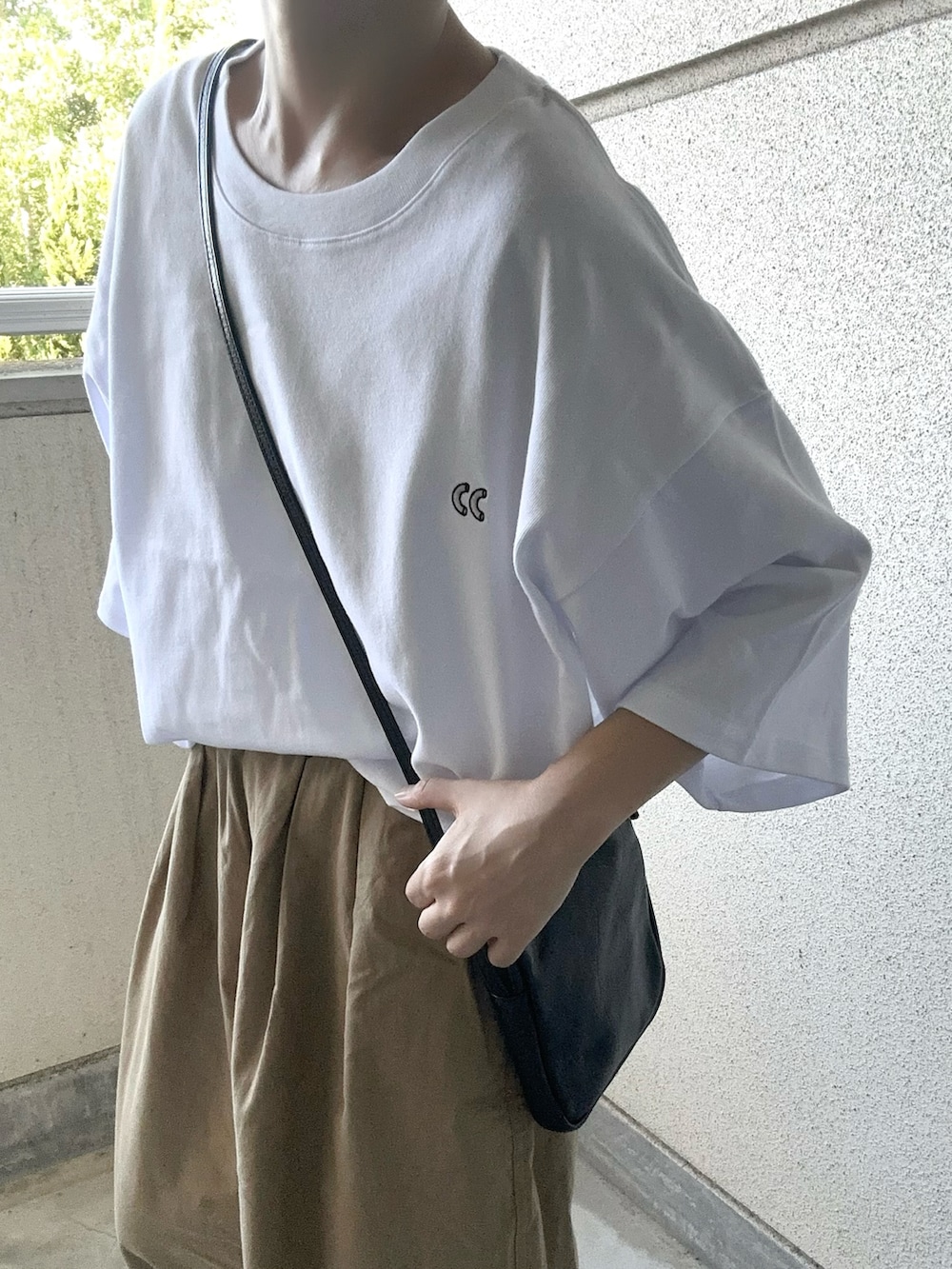 ホワイト系のTシャツ/カットソー、ベージュ系のチノパンツ、ブラック系のショルダーバッグを着用したレディースの夏コーディネートの2枚目の写真