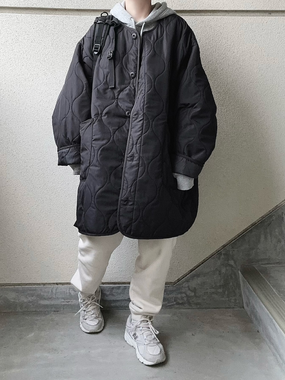 ブラック系のノーカラーコート、グレー系のパーカー、ホワイト系のスウェットパンツを着用したレディースの冬コーディネートの5枚目の写真