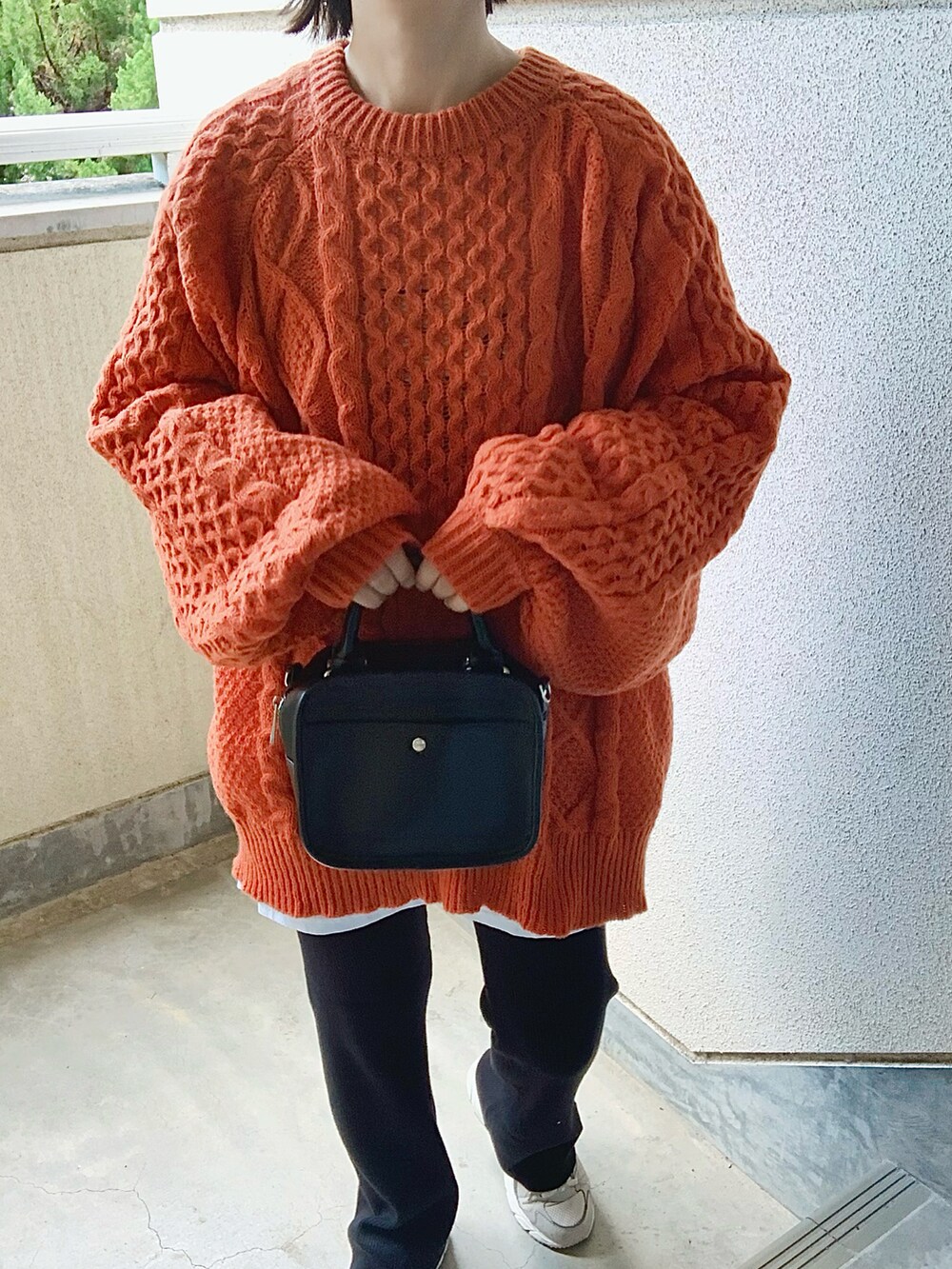 オレンジ系のニット/セーター、ブラック系のその他パンツ、グレー系のスニーカーを着用したレディースの秋コーディネートの2枚目の写真