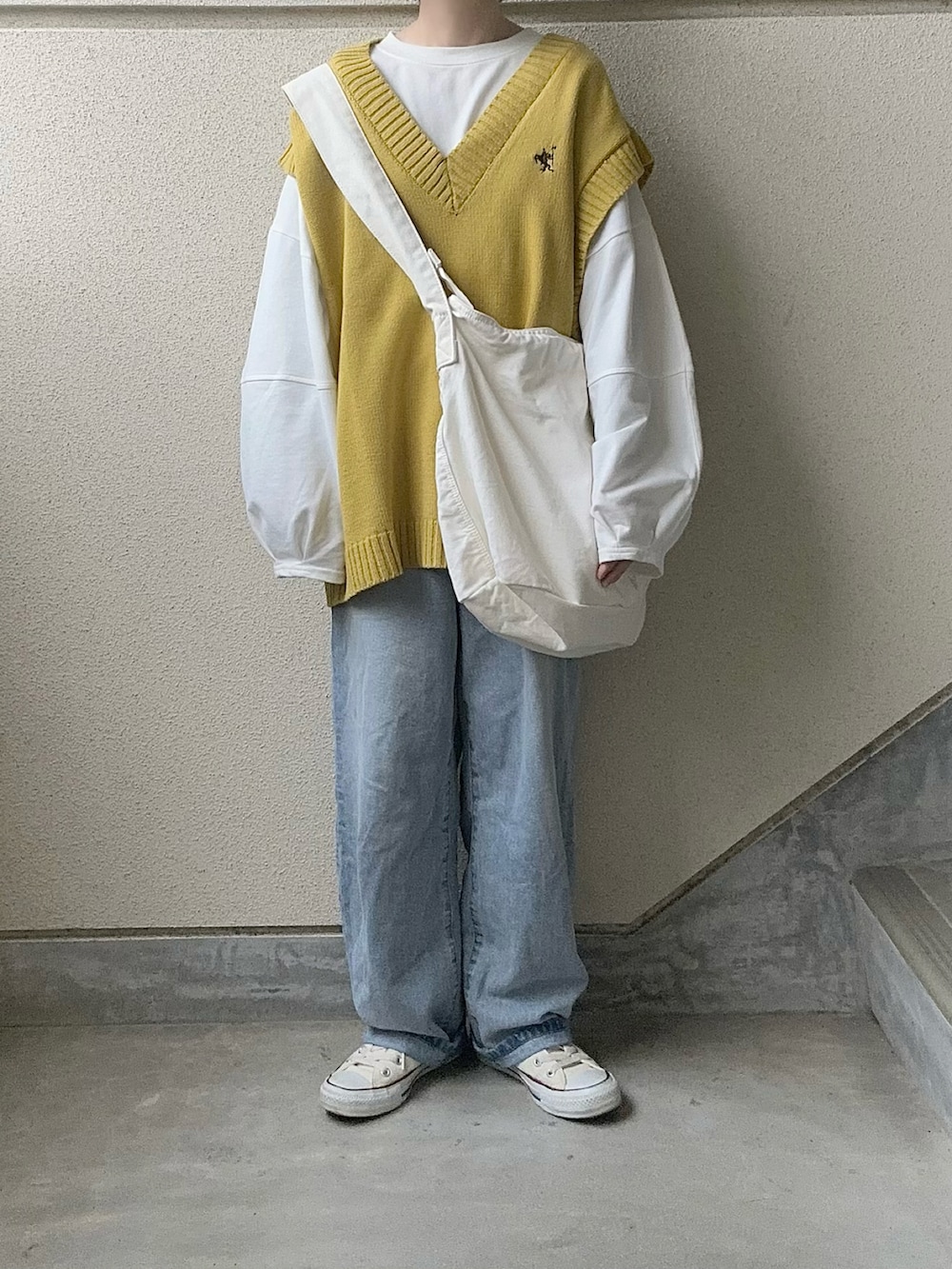 イエロー系のベスト、ブルー系のデニムパンツ、ホワイト系のショルダーバッグを着用したレディースの春コーディネートの3枚目の写真