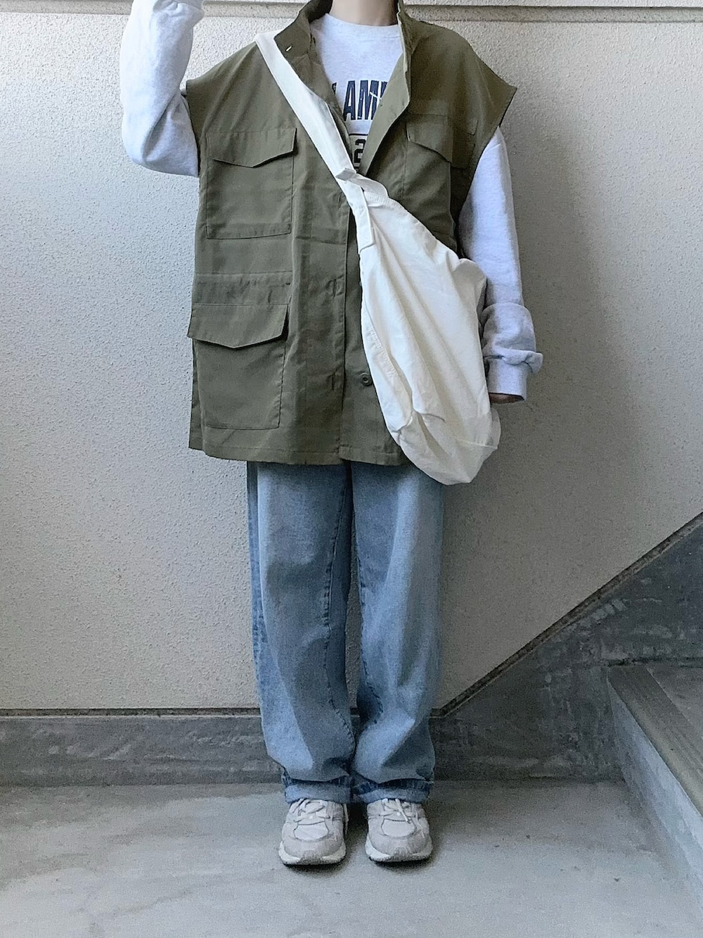 グリーン系のベスト、ブルー系のデニムパンツ、ホワイト系のショルダーバッグを着用したレディースの春コーディネートの2枚目の写真