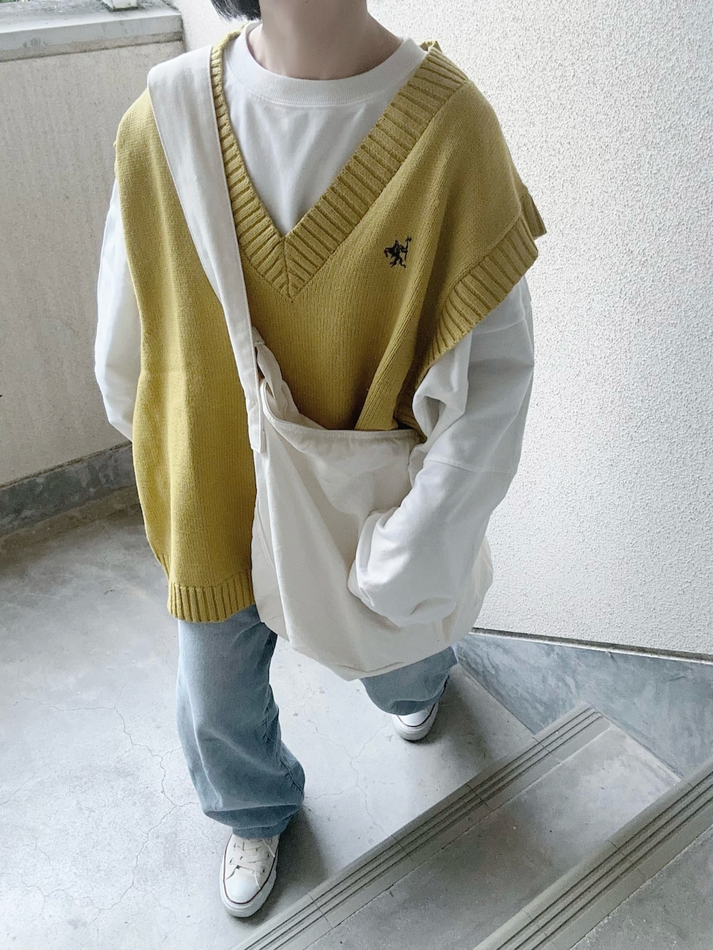 イエロー系のベスト、ブルー系のデニムパンツ、ホワイト系のショルダーバッグを着用したレディースの春コーディネートの4枚目の写真