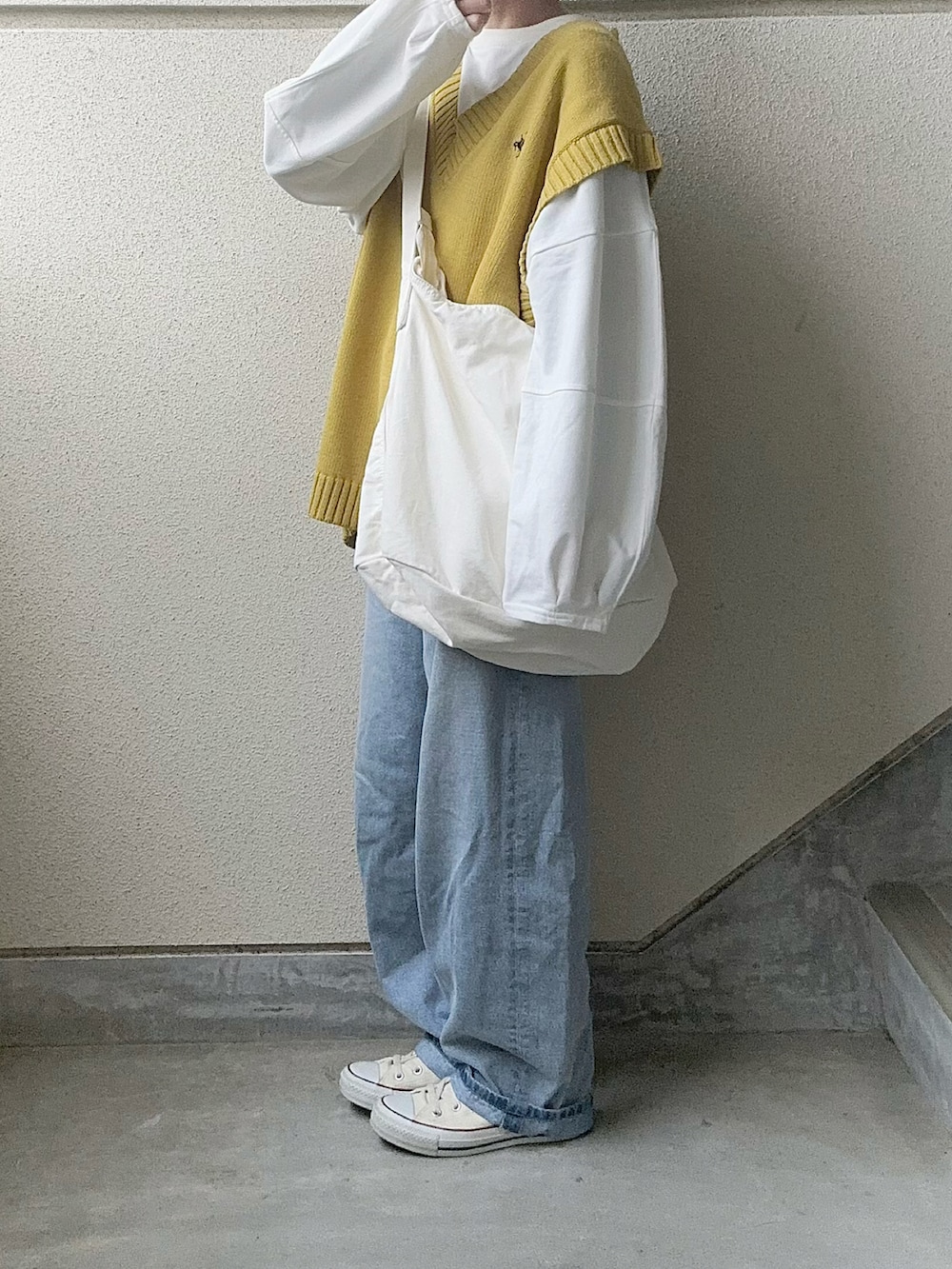 イエロー系のベスト、ブルー系のデニムパンツ、ホワイト系のショルダーバッグを着用したレディースの春コーディネートの2枚目の写真