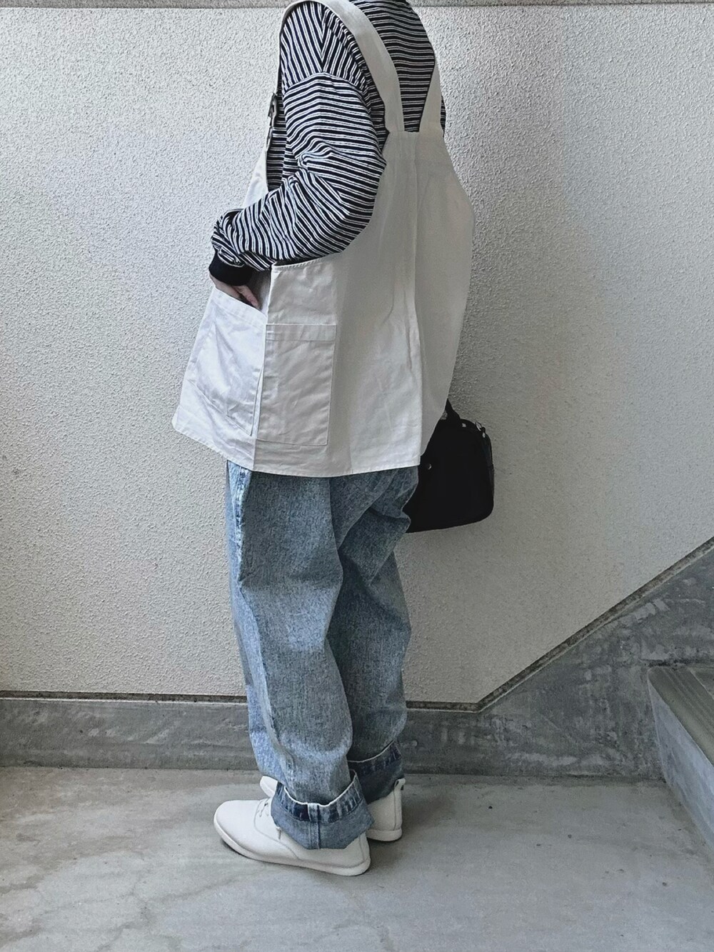 ブルー系のデニムパンツ、ホワイト系のベスト、ホワイト系のスニーカーを着用したレディースの春コーディネートの4枚目の写真