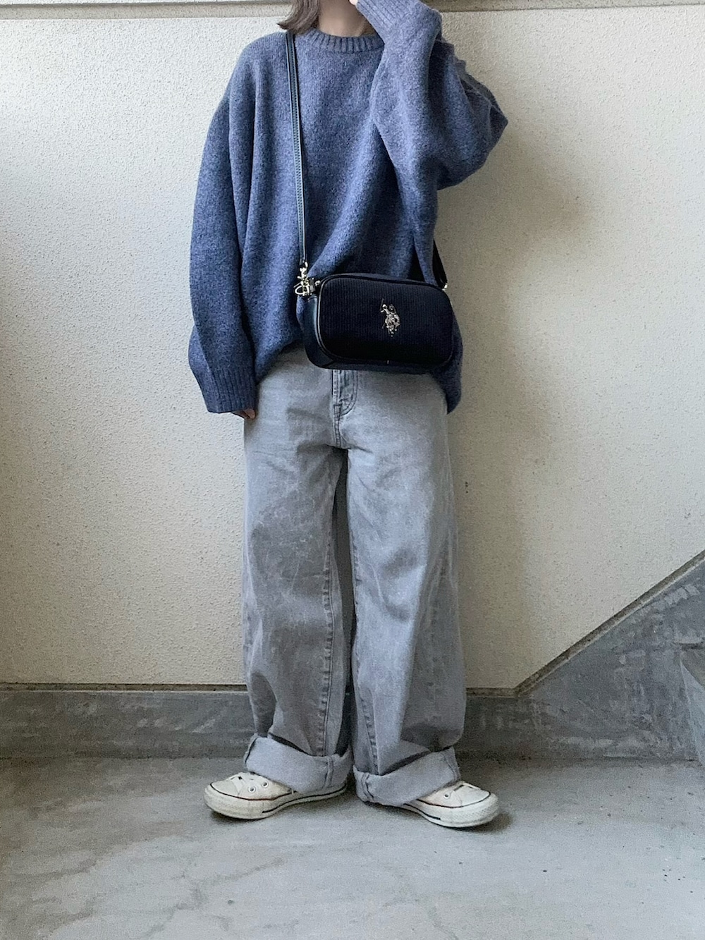 ブラック系のショルダーバッグ、ブルー系のニット/セーター、グレー系のデニムパンツを着用したレディースの秋コーディネートの2枚目の写真