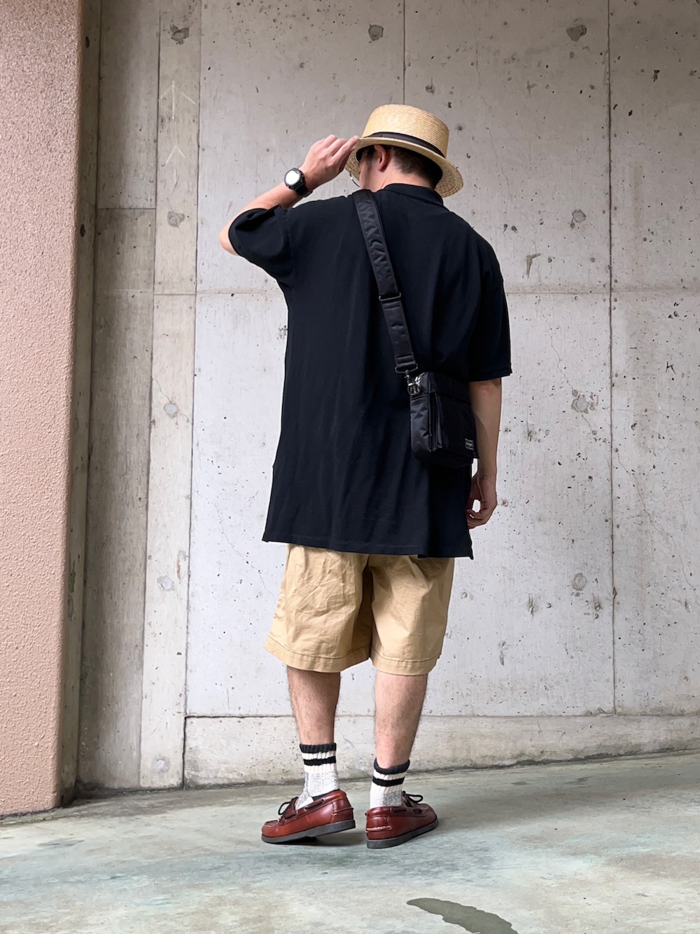 ブラック系のポロシャツ、ブラウン系のモカシン/デッキシューズ、ブラック系のショルダーバッグを着用したメンズの夏コーディネートの3枚目の写真