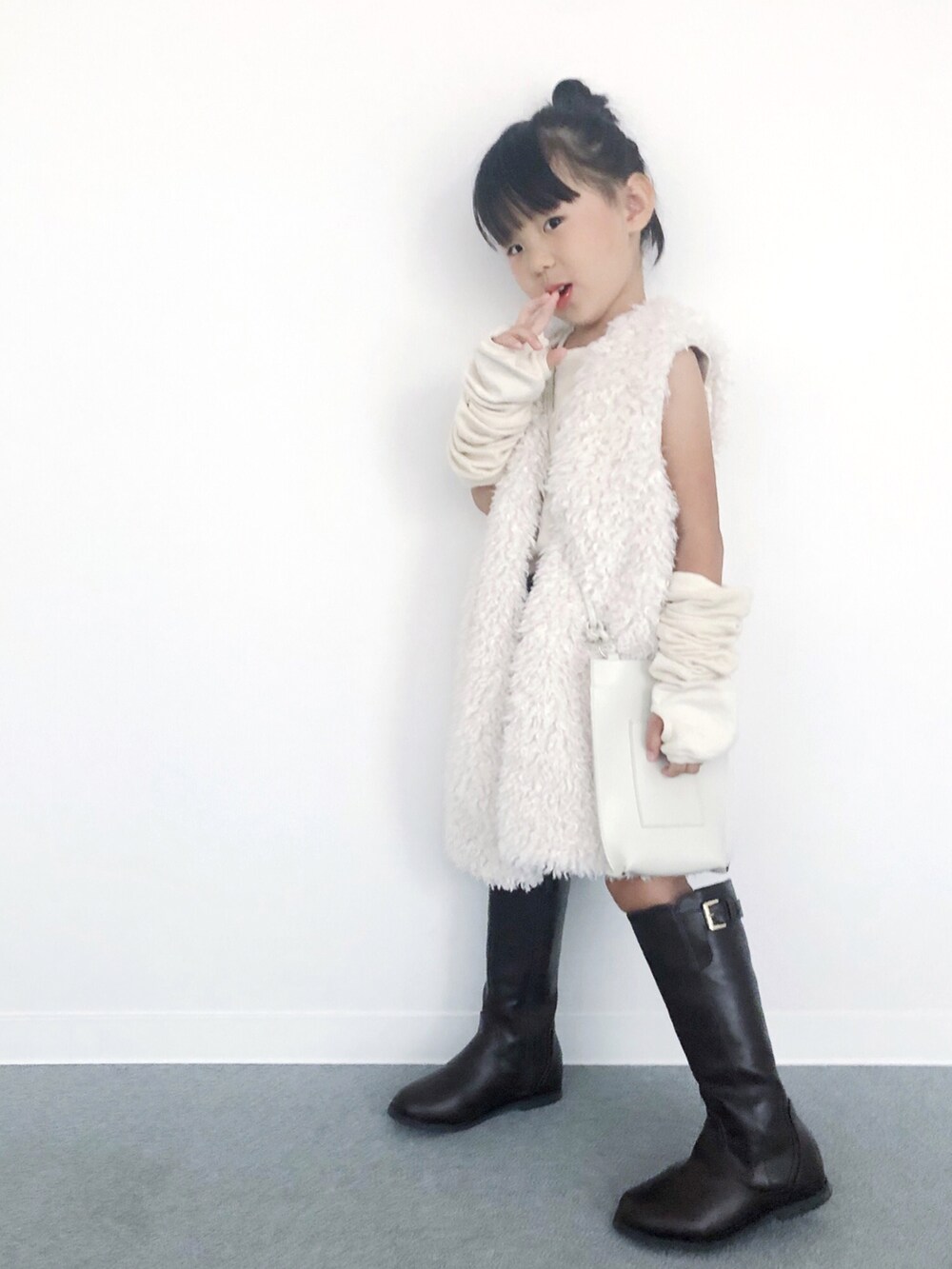 ブラウン系のブーツ、ホワイト系のショルダーバッグ、ホワイト系のベストを着用したキッズの秋コーディネートの2枚目の写真