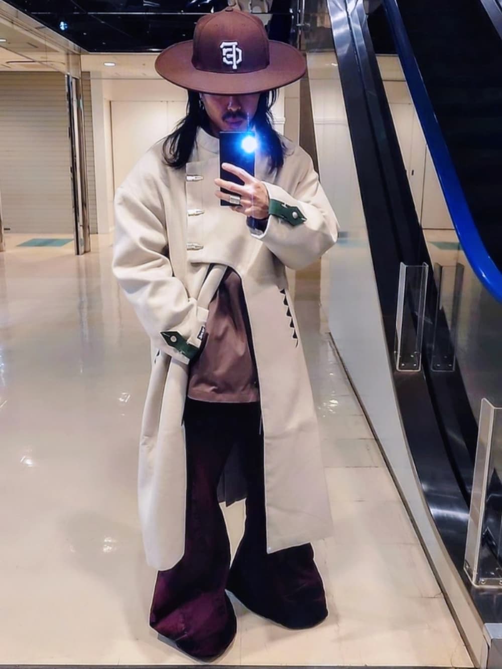 ベージュ系のノーカラーコート、ピンク系のデニムパンツ、ブラック系のブーツを着用したメンズの春コーディネートの2枚目の写真