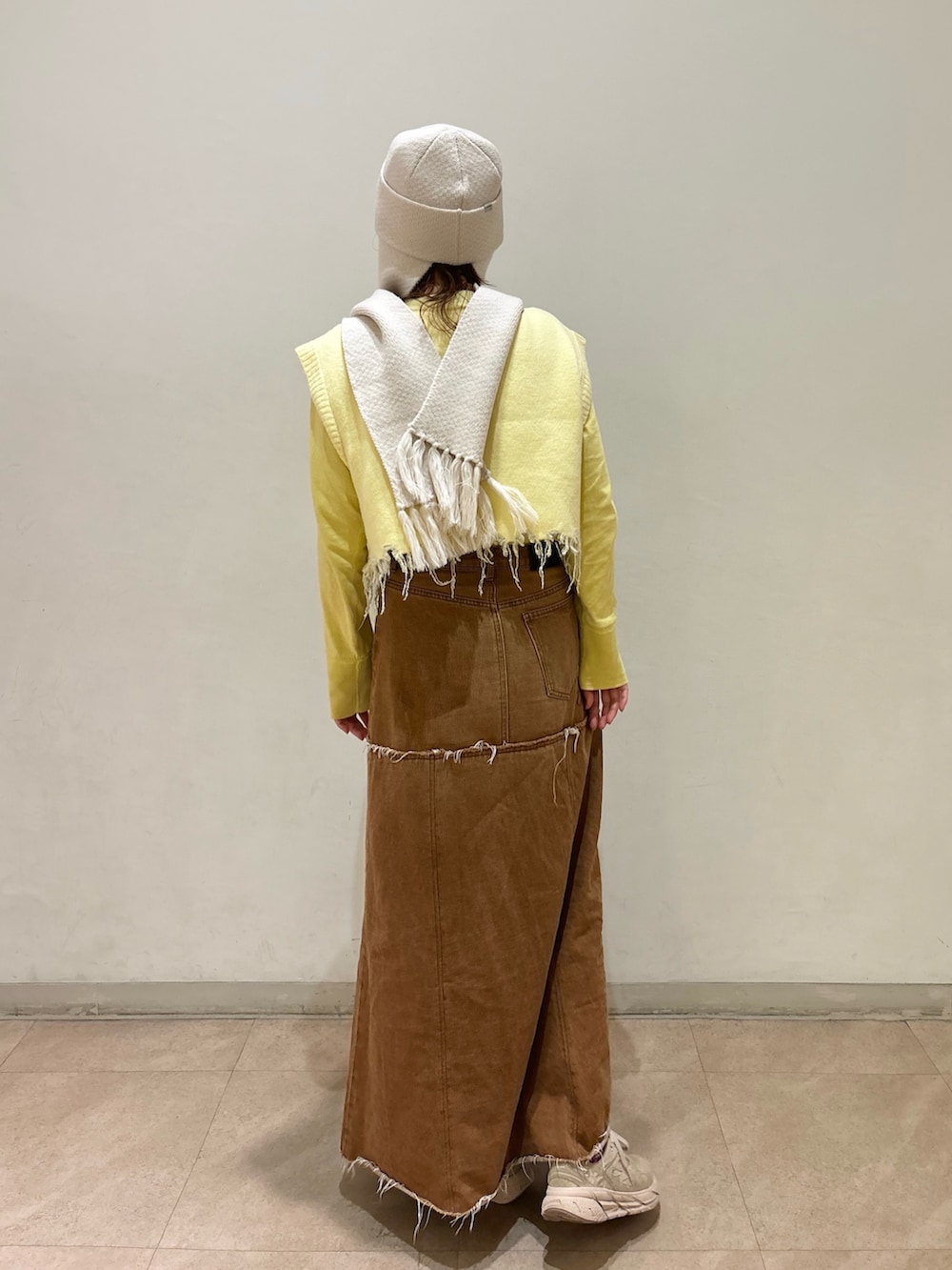 ブラウン系のデニムスカート、イエロー系のベスト、ベージュ系のスニーカーを着用したレディースの秋コーディネートの2枚目の写真