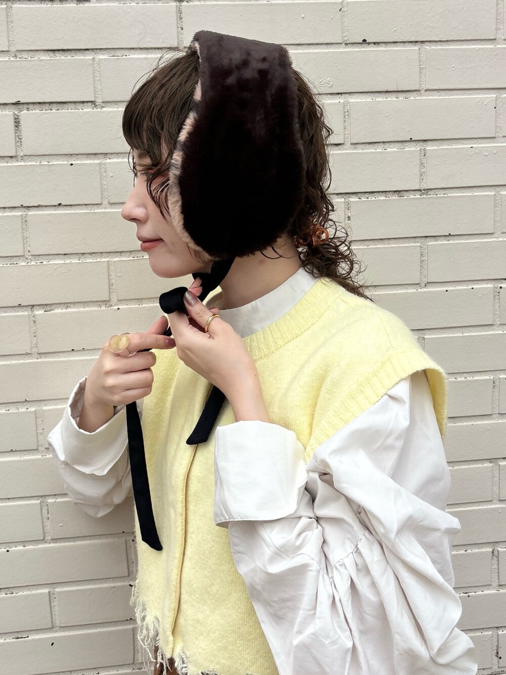 イエロー系のベスト、ブラウン系のデニムスカート、ブラウン系のサンダルを着用したレディースの秋コーディネートの4枚目の写真