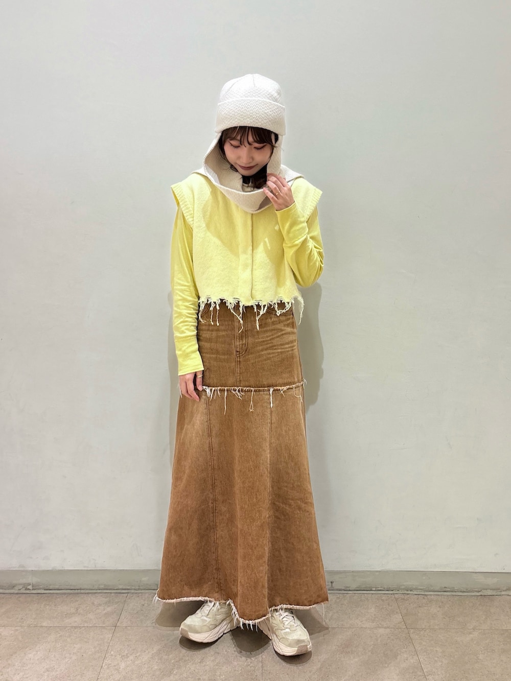 ブラウン系のデニムスカート、イエロー系のベスト、ベージュ系のスニーカーを着用したレディースの秋コーディネートの5枚目の写真