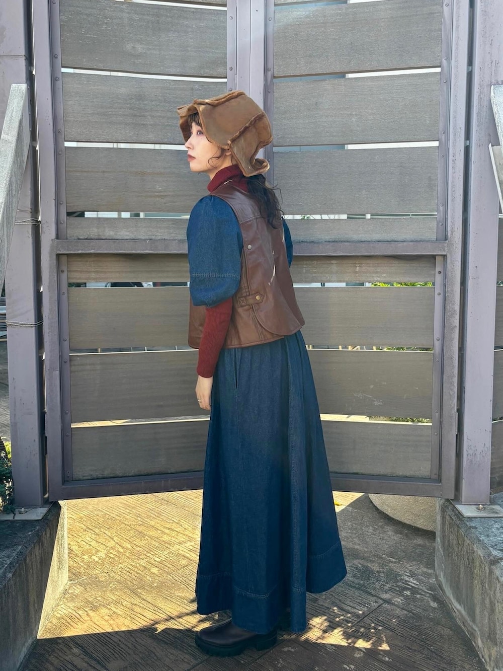 ブラウン系のベスト、ブルー系のワンピース、レッド系のトップスを着用したレディースの秋コーディネートの4枚目の写真