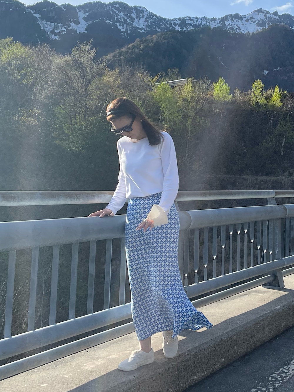 ブルー系のスカート、ホワイト系のショルダーバッグ、ホワイト系のスニーカーを着用したレディースの春コーディネートの2枚目の写真