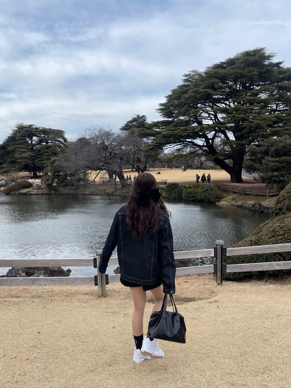 ホワイト系のスニーカー、ブルー系のデニムジャケット、ブラック系のハンドバッグを着用したレディースの冬コーディネートの2枚目の写真