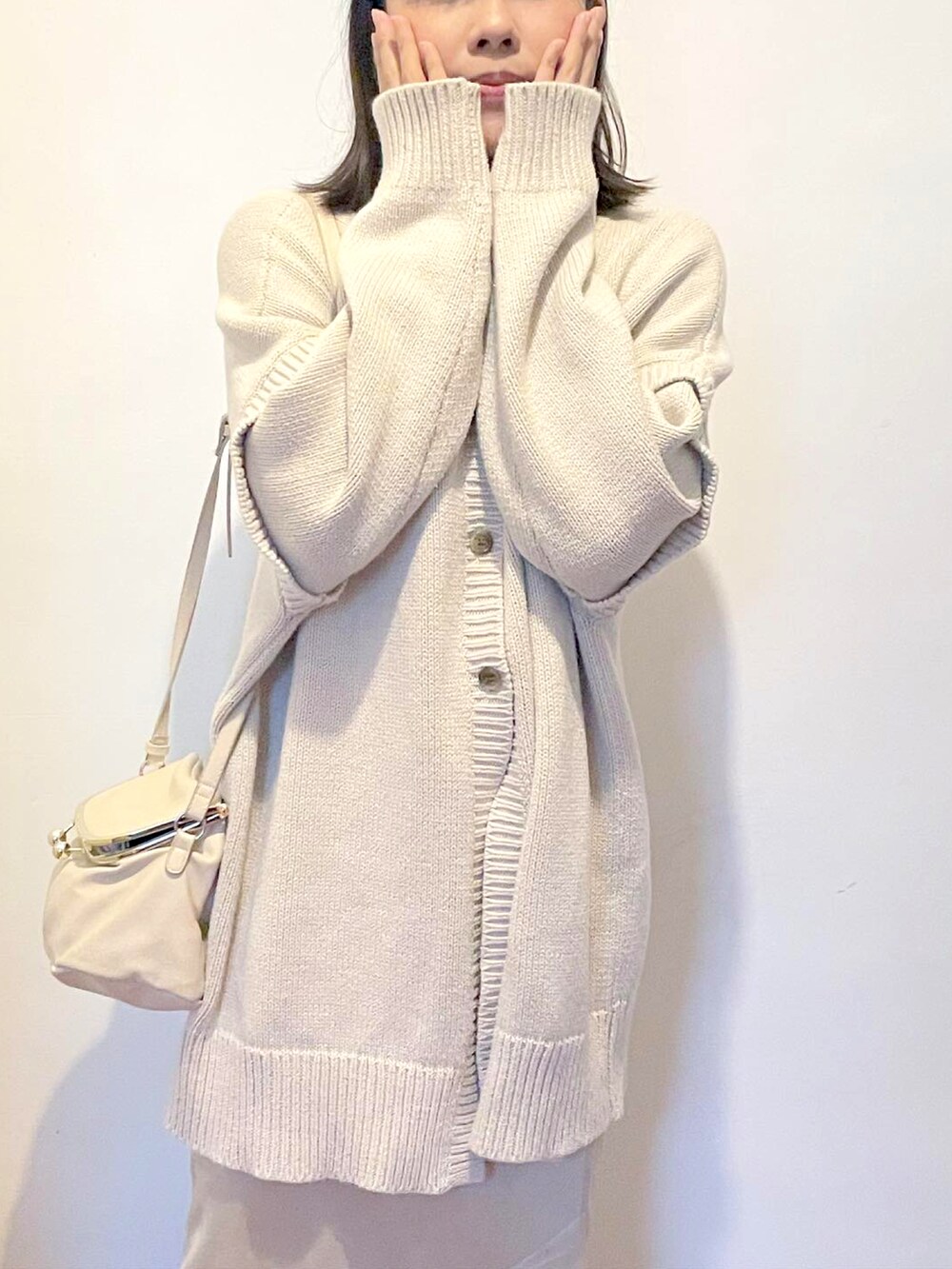 グレー系のニット/セーター、ベージュ系のスカート、ホワイト系のショルダーバッグを着用したレディースの冬コーディネートの2枚目の写真
