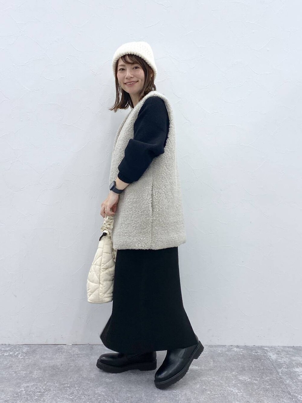 グレー系のベスト、ベージュ系のトートバッグ、ブラック系のブーツを着用したレディースの秋コーディネートの3枚目の写真