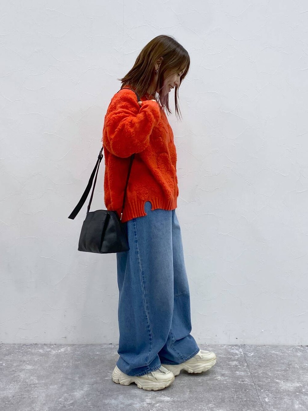 ブラック系のショルダーバッグ、レッド系のニット/セーター、ブルー系のデニムパンツを着用したレディースの冬コーディネートの5枚目の写真