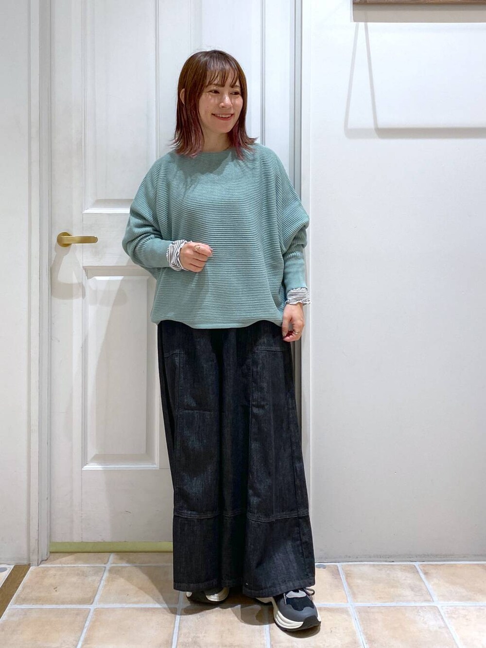 グリーン系のニット/セーター、ブルー系のデニムパンツ、ブラック系のスニーカーを着用したレディースの秋コーディネートの2枚目の写真