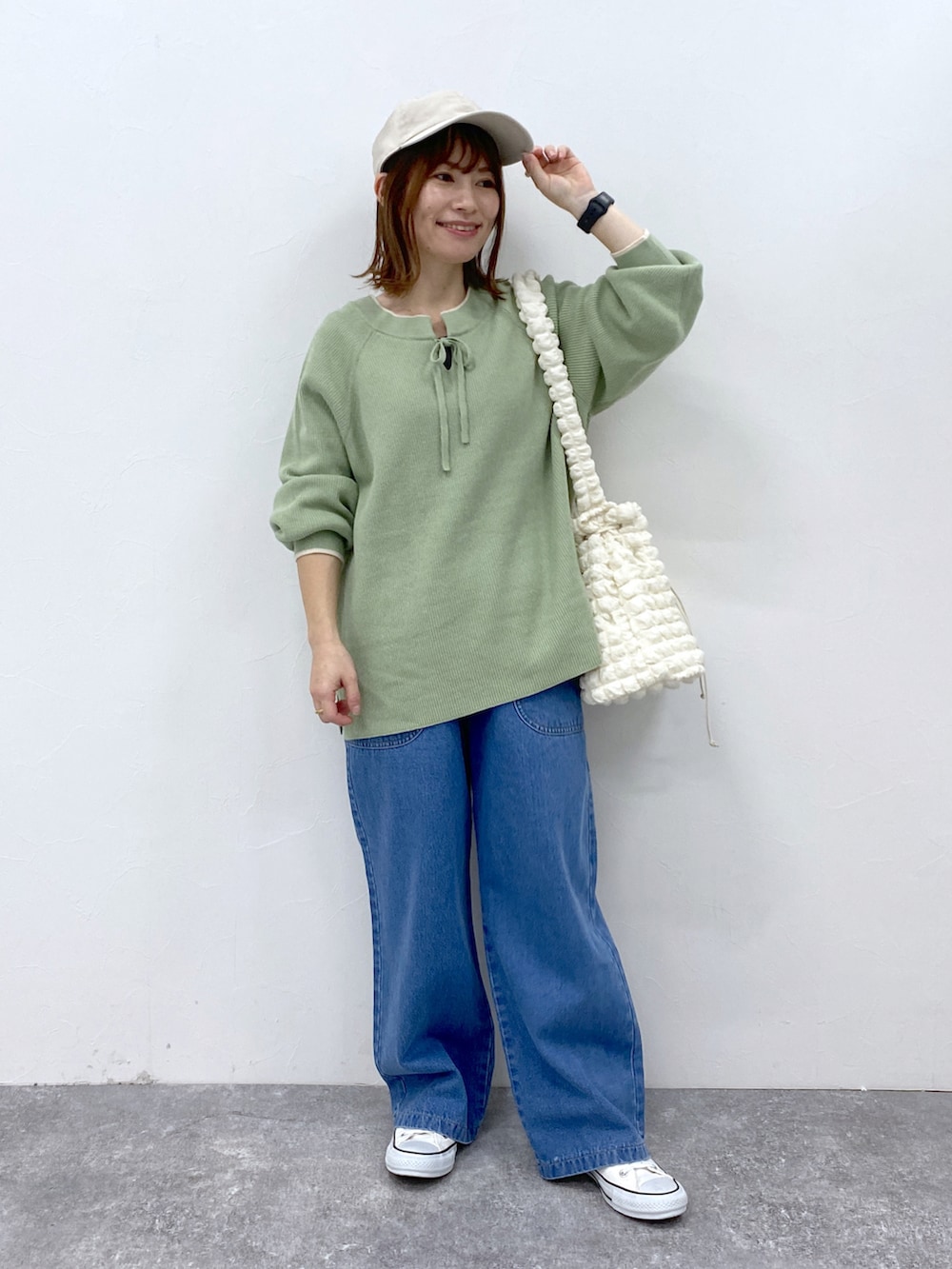 ブルー系のデニムパンツ、グリーン系のニット/セーター、ホワイト系のキャップを着用したレディースの冬コーディネートの2枚目の写真