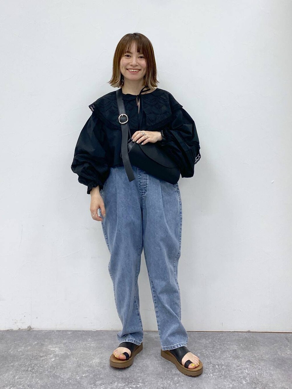 ブラック系のサンダル、ブルー系のデニムパンツ、ブラック系のショルダーバッグを着用したレディースの夏コーディネートの2枚目の写真