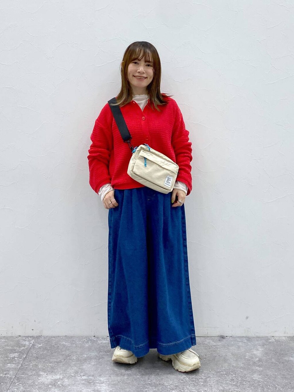 ベージュ系のショルダーバッグ、ブルー系のデニムパンツ、レッド系のカーディガン/ボレロを着用したレディースの春コーディネートの2枚目の写真