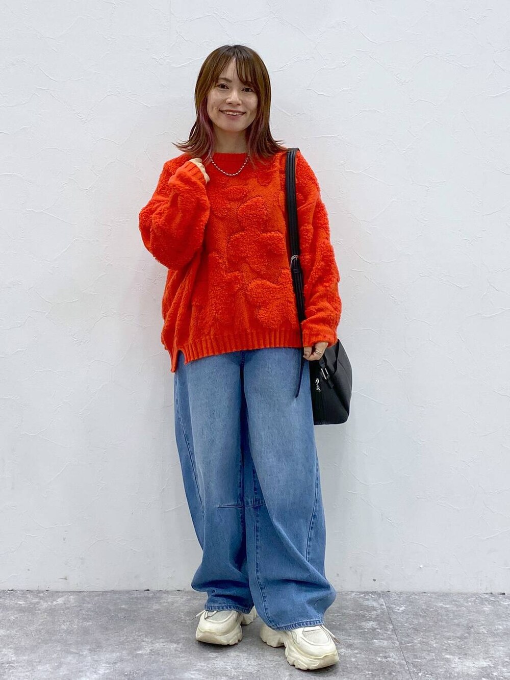 ブラック系のショルダーバッグ、レッド系のニット/セーター、ブルー系のデニムパンツを着用したレディースの冬コーディネートの4枚目の写真