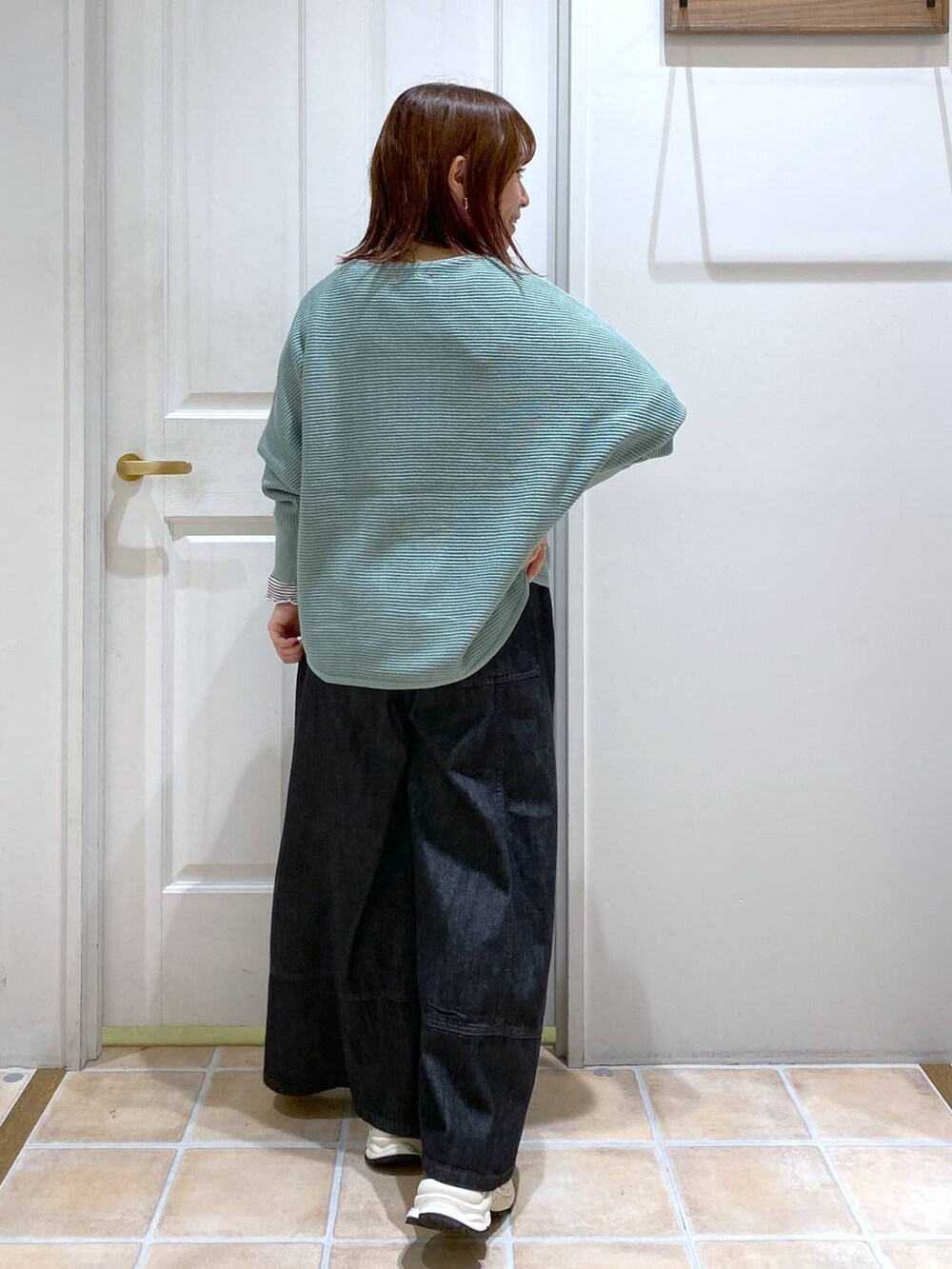 グリーン系のニット/セーター、ブルー系のデニムパンツ、ブラック系のスニーカーを着用したレディースの秋コーディネートの6枚目の写真