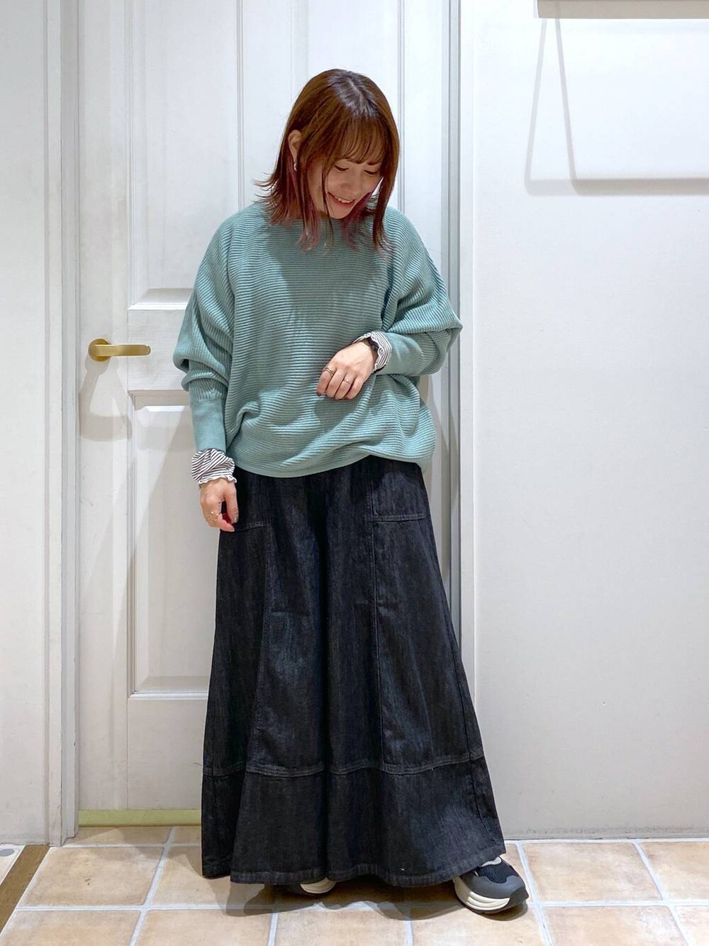 グリーン系のニット/セーター、ブルー系のデニムパンツ、ブラック系のスニーカーを着用したレディースの秋コーディネートの3枚目の写真