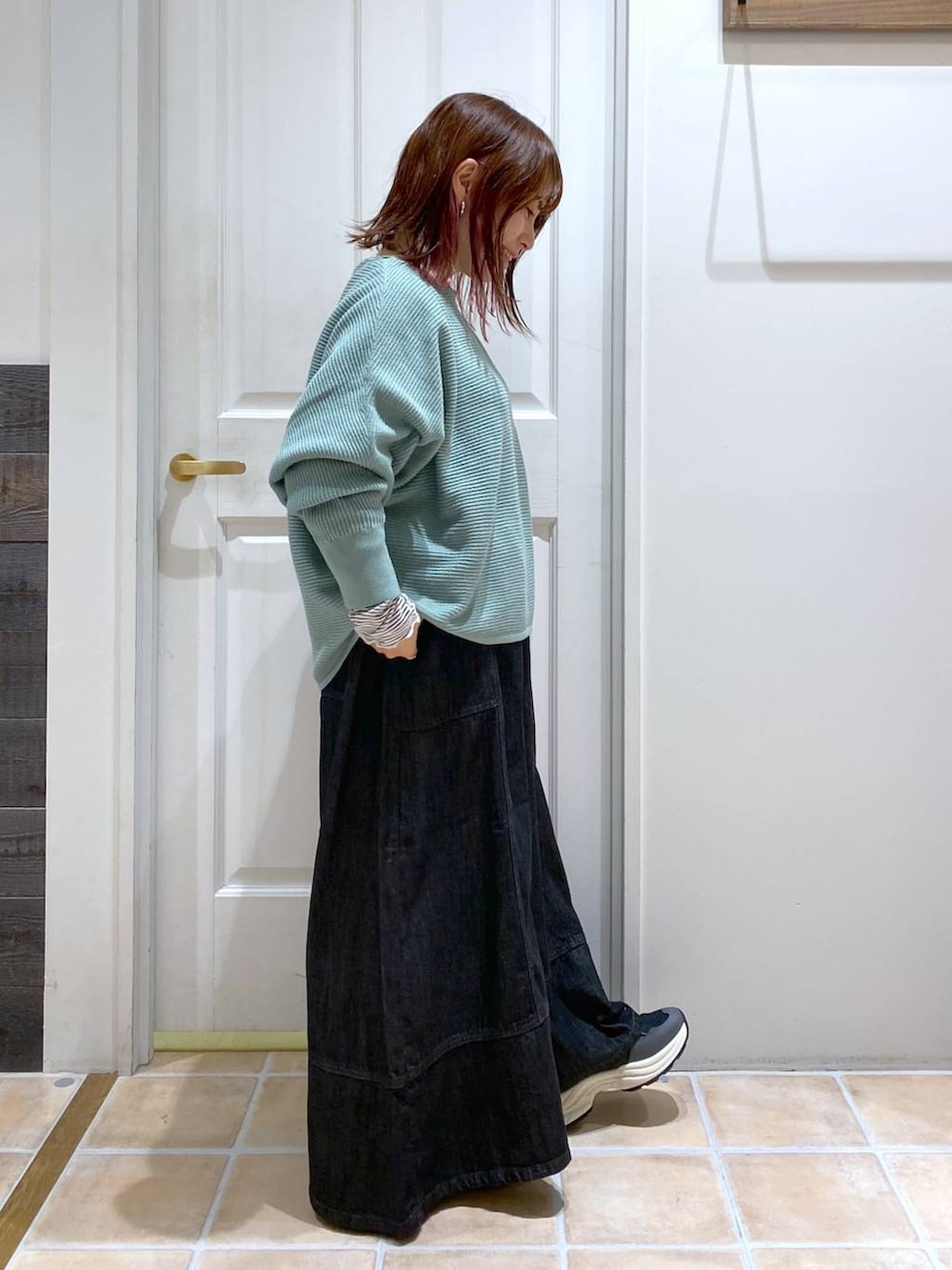 グリーン系のニット/セーター、ブルー系のデニムパンツ、ブラック系のスニーカーを着用したレディースの秋コーディネートの5枚目の写真