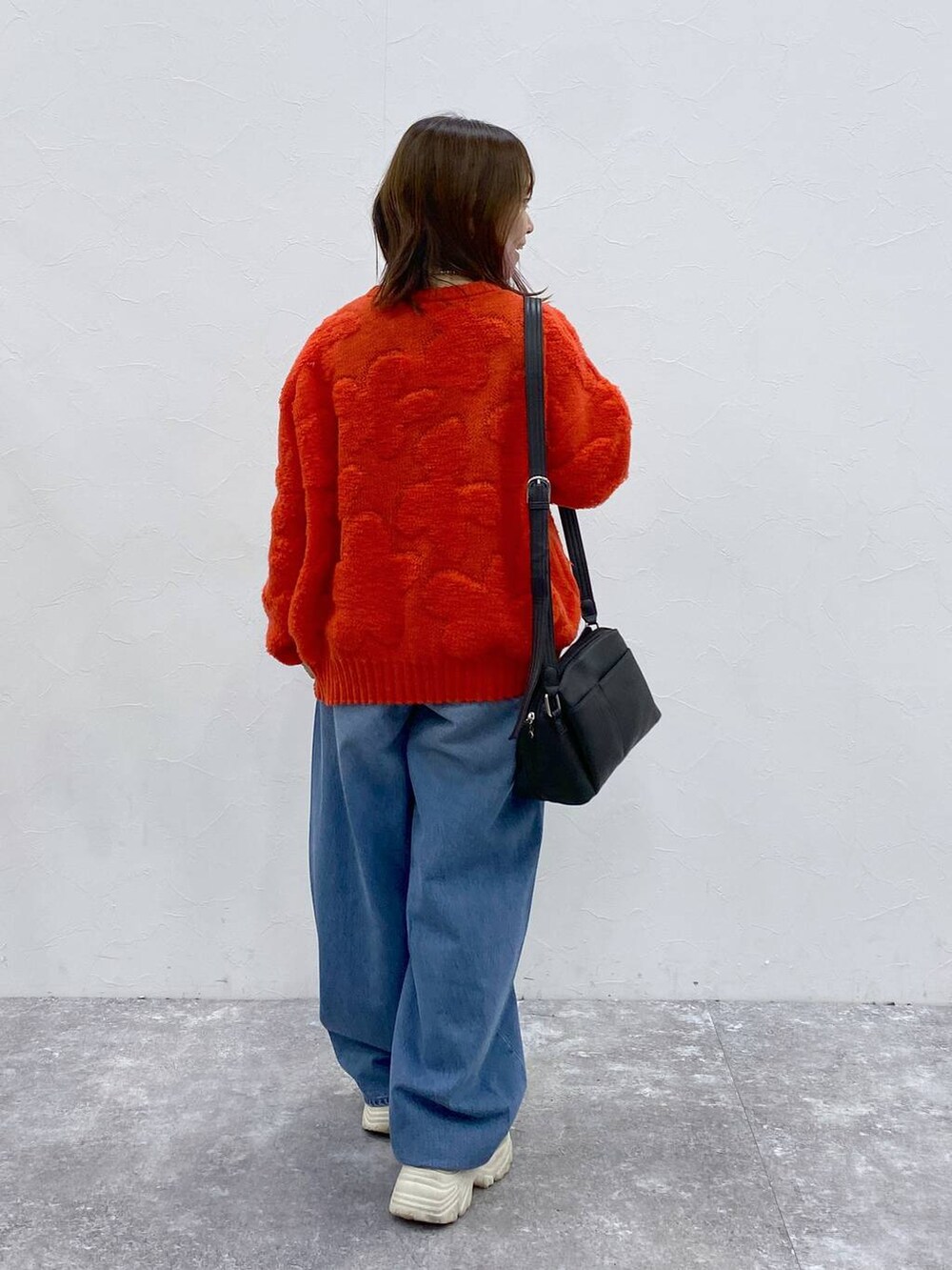 ブラック系のショルダーバッグ、レッド系のニット/セーター、ブルー系のデニムパンツを着用したレディースの冬コーディネートの6枚目の写真