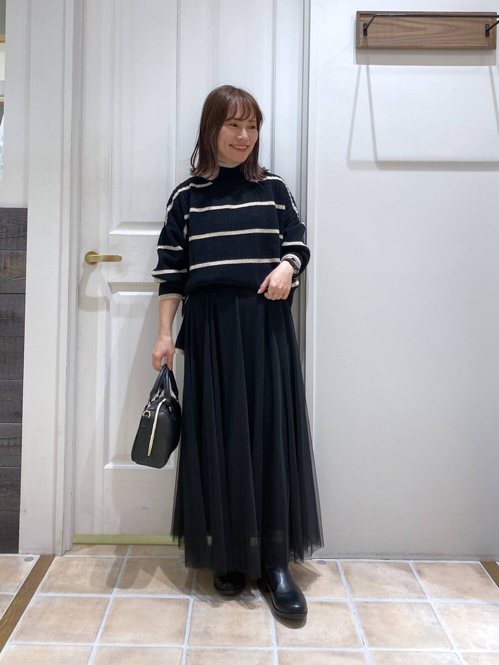 ブラック系のブーツ、その他のニット/セーター、ブラック系のスカートを着用したレディースの冬コーディネートの2枚目の写真