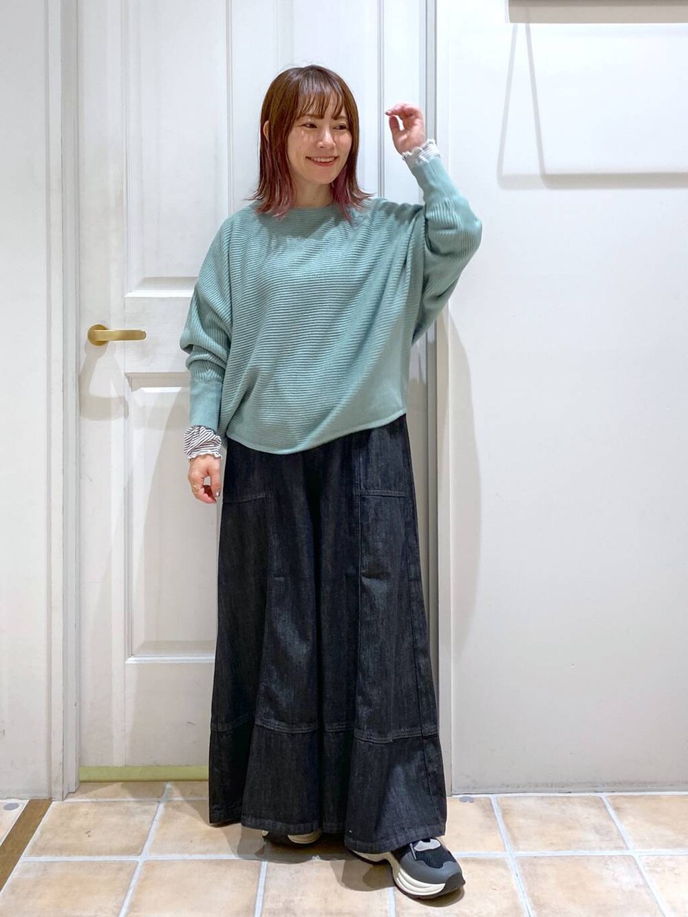 グリーン系のニット/セーター、ブルー系のデニムパンツ、ブラック系のスニーカーを着用したレディースの秋コーディネートの4枚目の写真