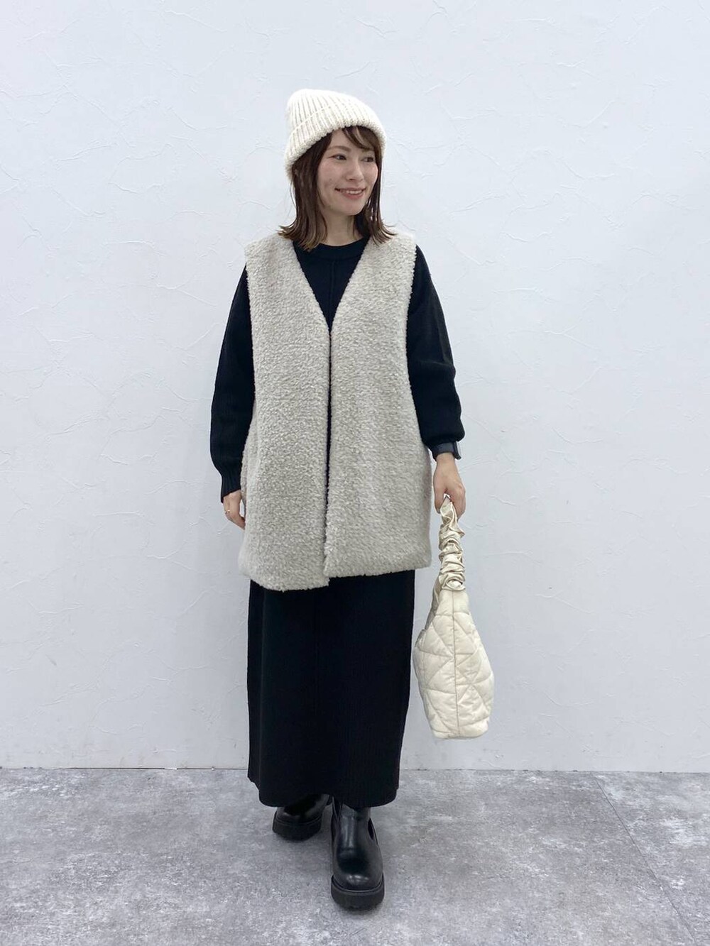 グレー系のベスト、ベージュ系のトートバッグ、ブラック系のブーツを着用したレディースの秋コーディネートの2枚目の写真