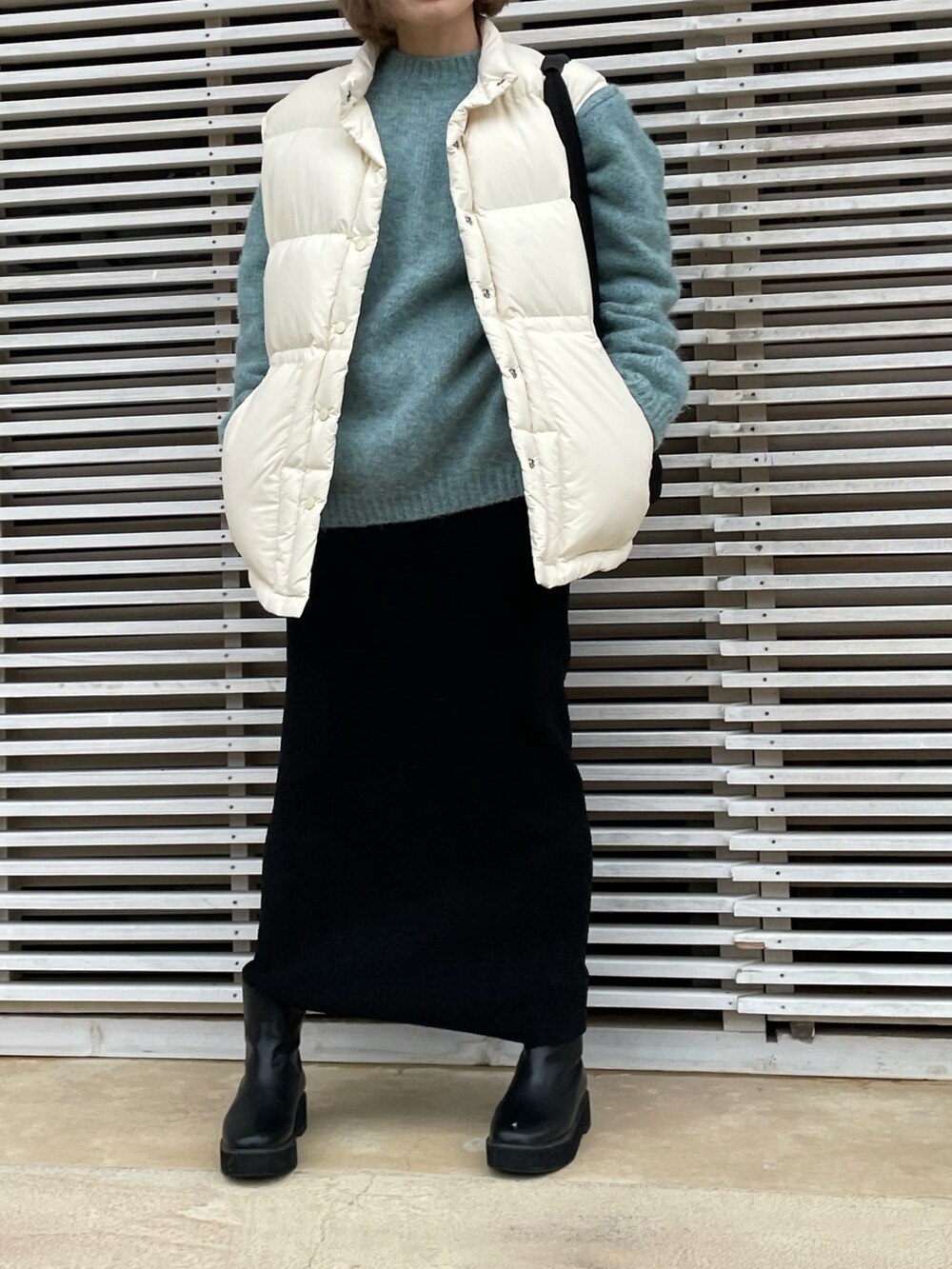 ブルー系のニット/セーター、ホワイト系のダウンベスト、ブラック系のスカートを着用したレディースの冬コーディネートの2枚目の写真