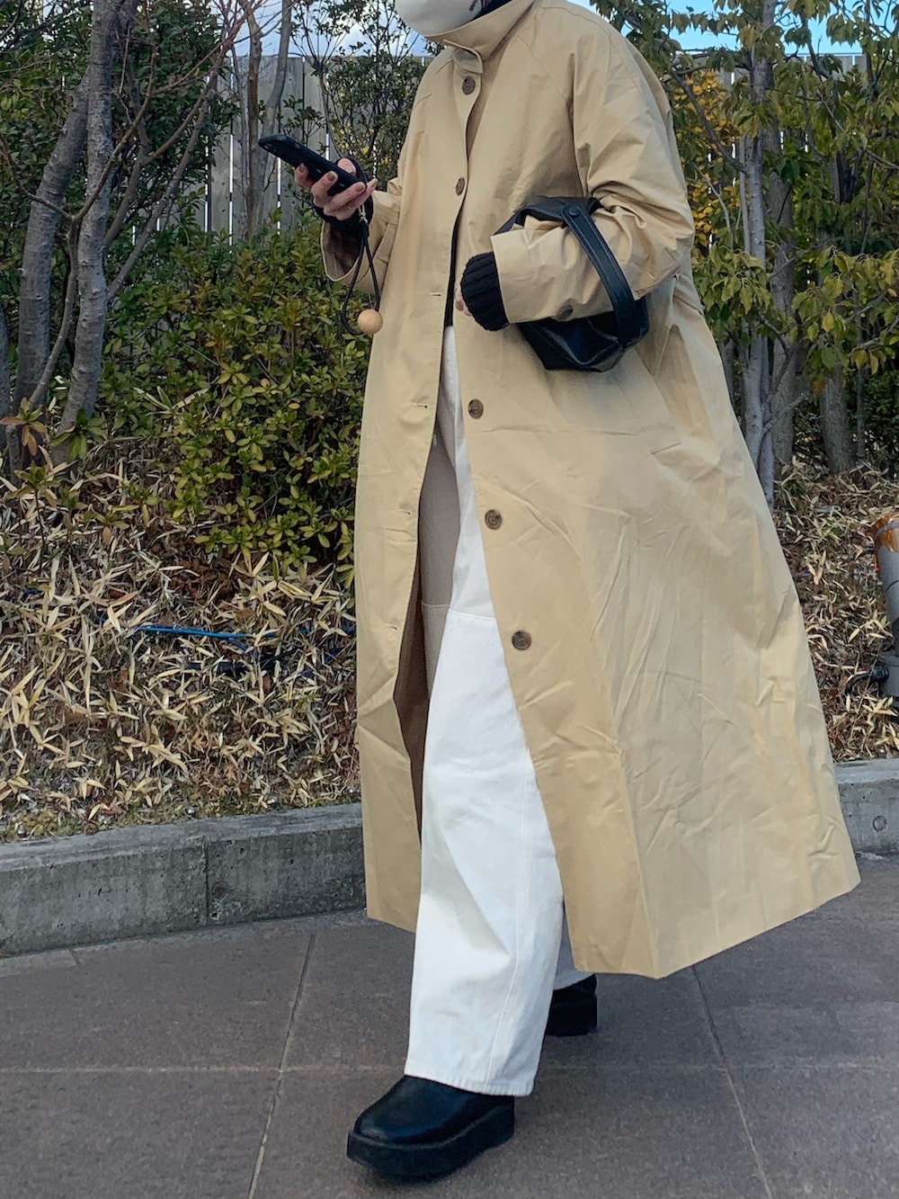 ベージュ系のトレンチコート、ブラック系のトートバッグ、ブラック系のニット/セーターを着用したレディースの冬コーディネートの2枚目の写真