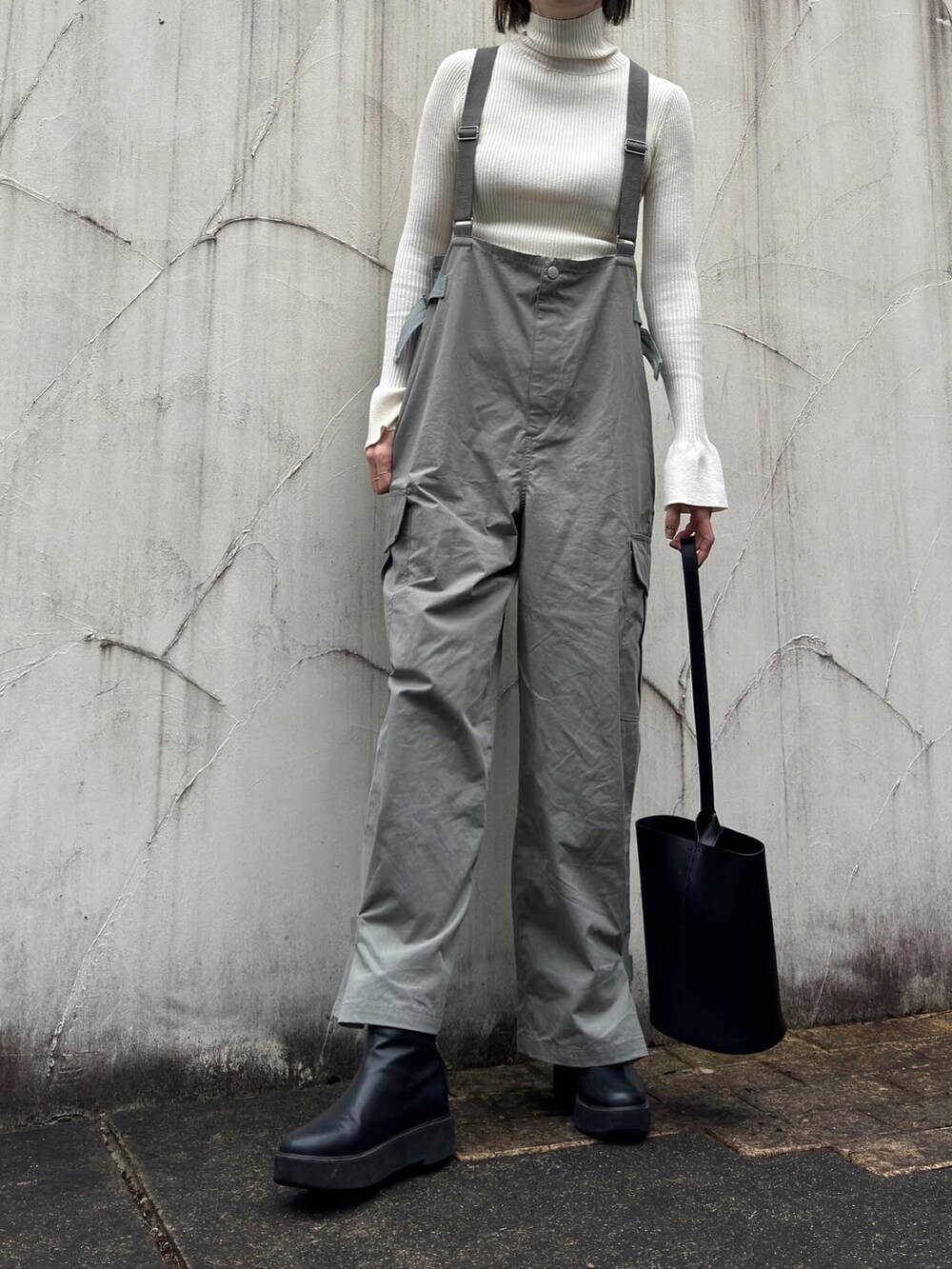 ホワイト系のニット/セーター、グリーン系のサロペット/オーバーオール、ブラック系のブーツを着用したレディースの冬コーディネートの2枚目の写真